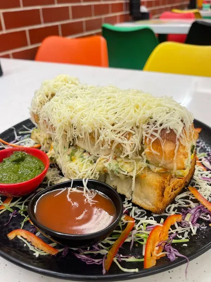 This is the Mumbai Bites Italian Sandwich, fully loaded and ready to be devoured. It's packed with a crunchy vegetable filling, multiple sauces, and a mountain of grated cheese, served with our signature chutneys.