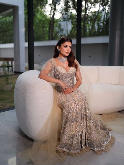 Seated gracefully, she looks like a true muse. The lighting highlights the impeccable blend of her makeup and the intricate details of her gown, creating a truly aspirational image.