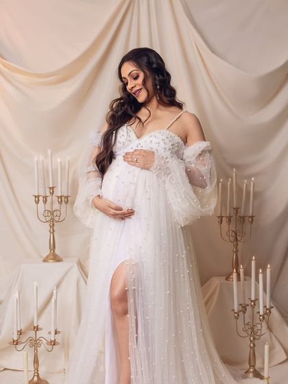 An angelic mom-to-be in a beautiful pearl-studded white gown, surrounded by the romantic glow of candles.