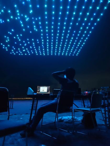 A pilot monitors the show from the ground console, surrounded by the blue glow of the drone formation. This image highlights the technology and human control behind every spectacle.