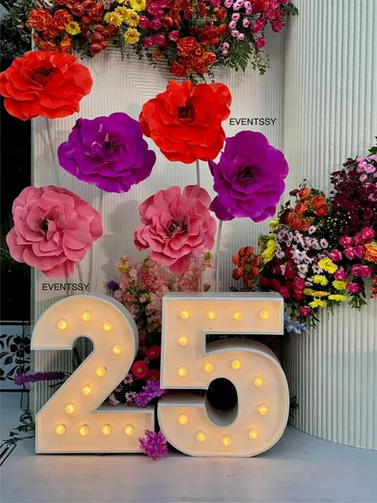 Another angle of the marquee numbers and oversized paper flowers. The combination of lighting and bold floral decor creates a festive and sophisticated atmosphere for an adult birthday celebration.