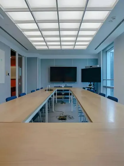 A spacious and technologically advanced boardroom designed for a corporate office in Gurgaon. The design prioritizes functionality with integrated AV systems, ample natural light, and a large U-shaped table to facilitate effective meetings for large teams.