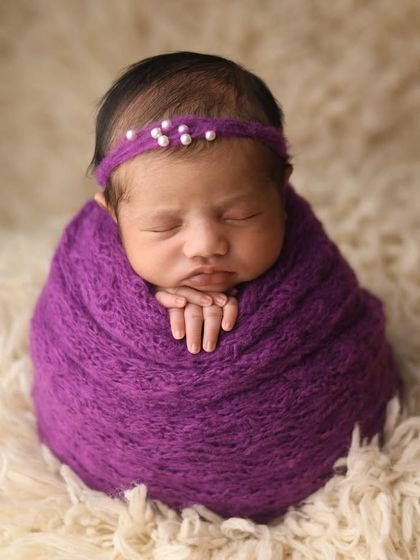 A close-up of the classic potato sack pose. The rich purple wrap and delicate pearl headband create a beautiful colour contrast against the soft, cream-coloured rug.