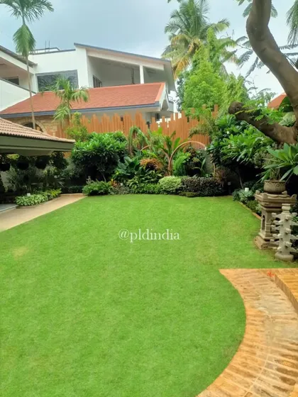 A view across the lawn in a Juhu residence. The garden features a mix of open lawn, sculptural elements, and dense perimeter planting to create a varied and interesting landscape.