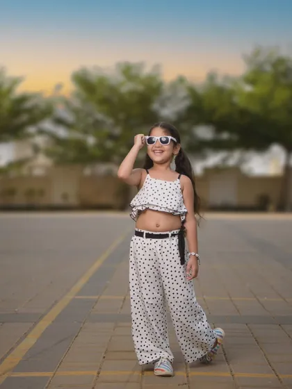 An outdoor shot capturing a carefree, sunny day vibe. Her polka-dot outfit and white sunglasses give off a cool, retro feel. This photo shows how we can take stylish portraits outside the studio, using natural light and settings.