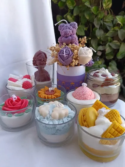 This image displays a variety of my whipped and dessert candles. You can see the different styles, from a yellow dessert candle with waffles and macarons to a sunflower-themed jar and a classic rose design.