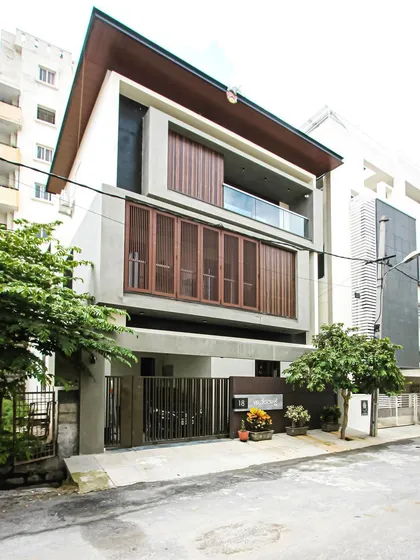 The 'Ananthaksha' residence, featuring custom-designed movable wooden screens. These shutters provide residents with control over privacy and sunlight while adding a dynamic, textured element to the contemporary concrete facade.