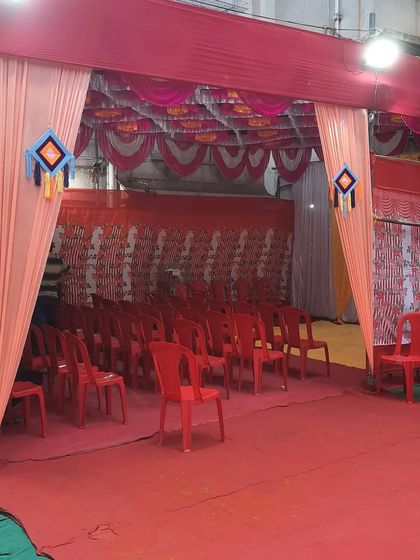 The entrance to a pandal setup for a Haldi event, with red chairs neatly arranged for the guests.