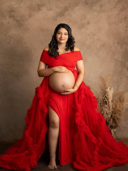 This portrait showcases a beautiful bare bump, celebrating the incredible transformation of a mother's body. The rich red gown frames the moment perfectly against a classic studio backdrop.