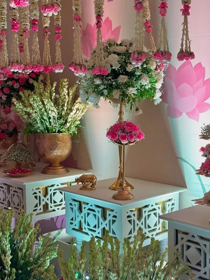 A close-up of the decor details, including a floral centerpiece on a tall golden stand and a backdrop of hanging flower strings. The lotus motif on the wall adds a traditional touch.
