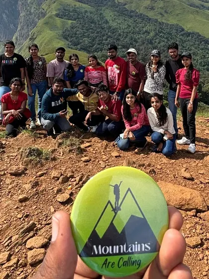 A guide proudly displays the "Mountains Are Calling" badge, with a happy group and a stunning mountain backdrop.