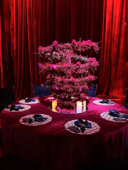 A dramatic tablescape with a tall, sculptural red cherry blossom centerpiece on a table draped in rich red velvet, embodying pure opulence.