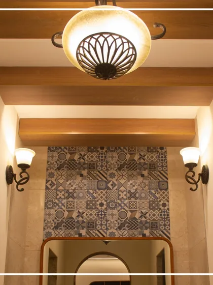 The lighting design in the gents' washroom combines a traditional chandelier with classic wall sconces. This layered approach provides both ambient and task lighting while reinforcing the modern heritage theme.