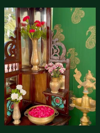 A corner vignette with a mirrored wooden shelf, brass vases holding fresh flowers, and a green paisley backdrop, showcasing detailed styling.