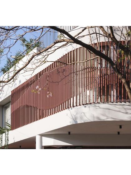 A closer look at the elegant curve of the 'House Under Tabebuia Trees' facade. The clean white cantilevered slab contrasts beautifully with the warm, earthy tone of the parametric screen.
