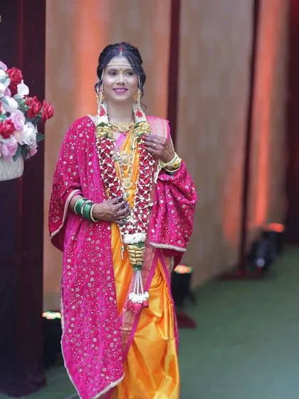 A full-length shot of the bride, looking elegant and ready for her ceremony. The vibrant colors of her saree and shawl are beautifully balanced by the soft, glowing makeup.
