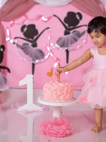 A little ballerina carefully places the 'one' candle on her cake, ready for her first birthday celebration.