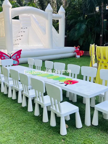 A full view of an outdoor party setup, featuring a long table with our white chairs and a large white bouncy castle in the background. This combination is perfect for garden parties and birthdays.