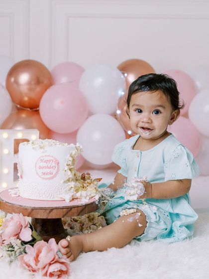 A happy baby girl enjoying her cake smash. Her smile and messy hands are the perfect picture of a successful first birthday celebration.