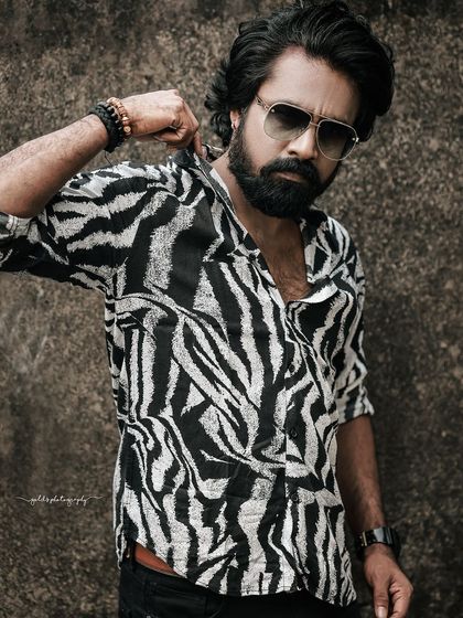 A stylish portrait of actor Swaraj Shetty, known for his role in 'Kanthara'. The zebra-print shirt and confident pose create a bold and fashionable look.