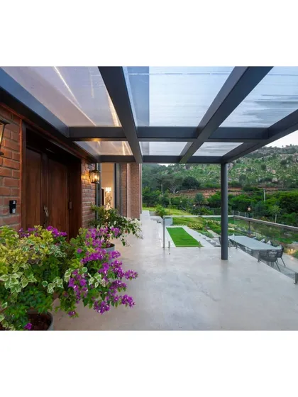 A view from the covered patio of the Nandi Hills home, looking out over the terraced garden towards the hills. The design uses a glass railing to ensure an unobstructed view, making the landscape the main focus.