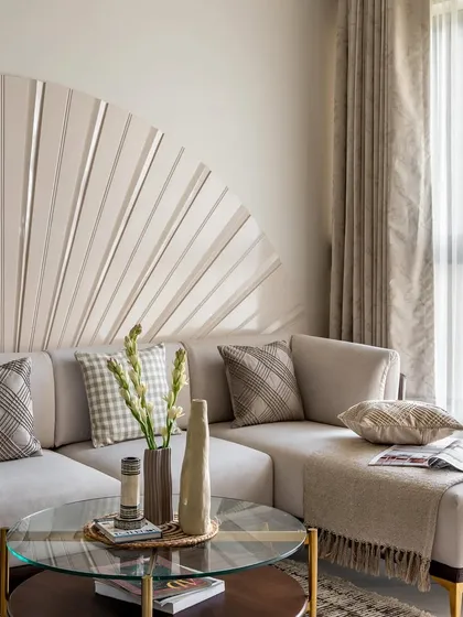 A close-up of the L-shaped sectional, showcasing how a unique fan-like wall feature can serve as art. The neutral palette is kept interesting with a mix of checkered and solid cushions, adding subtle texture.