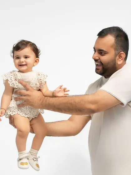 A proud father holds his smiling baby girl. The simplicity of the studio setting allows the beautiful connection between them to be the main focus.