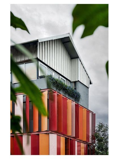 A duplicate image of the red facade building, showing its relationship with the surrounding trees.