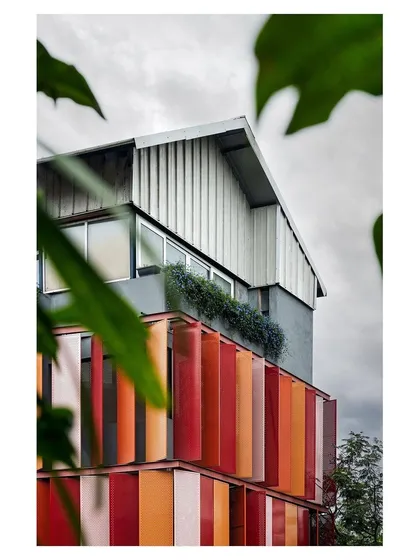 A duplicate image of the red facade building, showing its relationship with the surrounding trees.