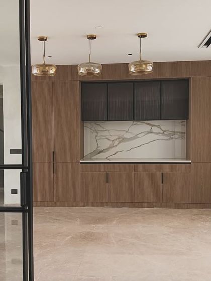 This custom-built crockery unit features a mix of materials, including wood-grain laminate, fluted dark wood cabinets, and a stunning marble backsplash. Three pendant lights highlight the unit, turning it into a feature wall.