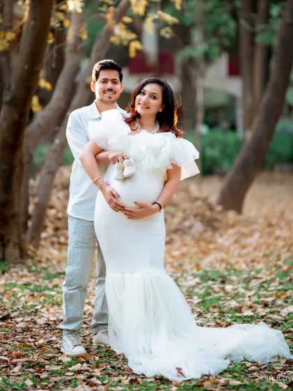 A beautiful family portrait in the making. Here, the couple holds up tiny baby shoes, a sweet symbol of the little one they are eagerly awaiting. This is a classic outdoor pregnancy announcement photo.