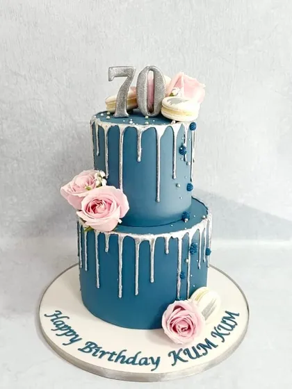 A sophisticated drip cake for a 70th birthday. The deep blue fondant is complemented by a silver drip, fresh pink roses, and delicate macarons.