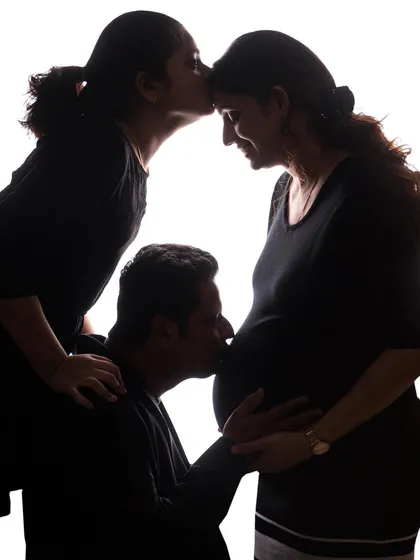 Welcoming a new baby is a moment for the whole family. This artistic silhouette maternity photo shows an older sibling and father sharing their love for the new arrival, creating a powerful family memory.