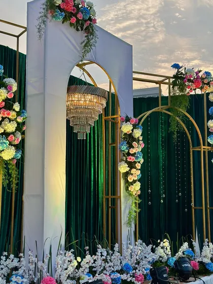 An elegant stage setup with gold-framed arches, a large chandelier, and emerald green drapes, perfect for a sophisticated wedding reception.