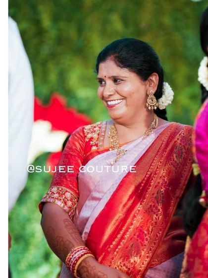 A smiling client dressed for a wedding celebration. She is wearing a custom red blouse with gold embroidery on the sleeves, a classic and elegant choice to pair with her traditional silk saree.