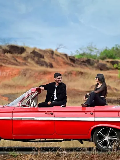 A cinematic pre-wedding portrait using a vintage red convertible as a prop. This shoot captures a cool, editorial vibe against a rustic, open-road backdrop, perfect for couples wanting a unique and stylish session.
