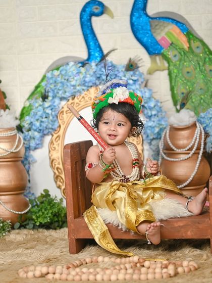 A smiling Little Krishna sitting on a small wooden bench, ready to play his flute.