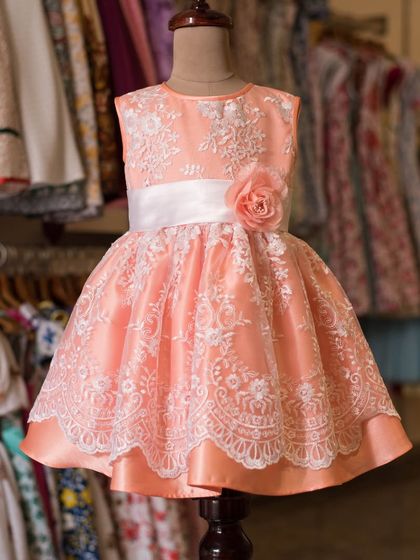 This peach dress is a masterpiece of lacework. The intricate white lace overlay creates a stunning pattern, and the satin sash with a rose adds a final touch of elegance.