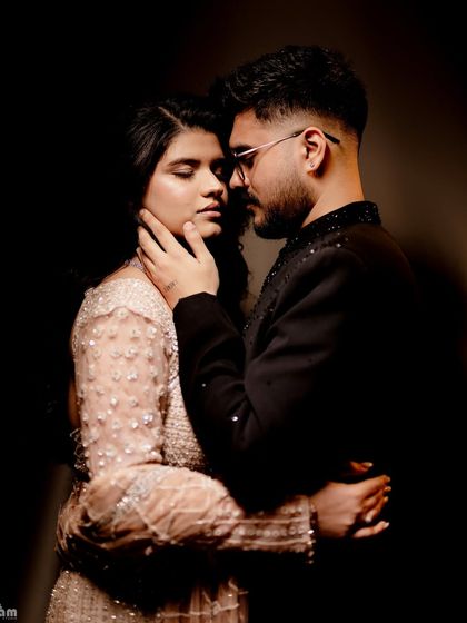 A dramatic and intimate studio portrait using chiaroscuro lighting. The deep shadows and focused light create a moody and passionate atmosphere, emphasizing the couple's intense connection.