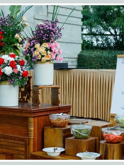 A beautifully arranged salad and condiment bar with fresh ingredients in glass bowls, set against a backdrop of elegant wooden furniture and floral decor.