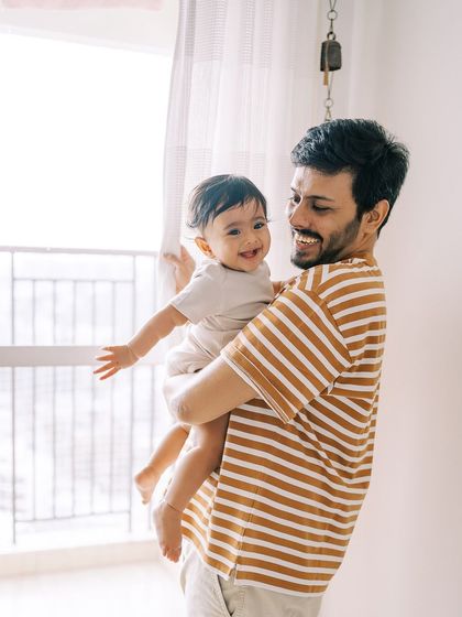 A father holding his smiling baby by the window. The natural light creates a beautiful, soft glow.