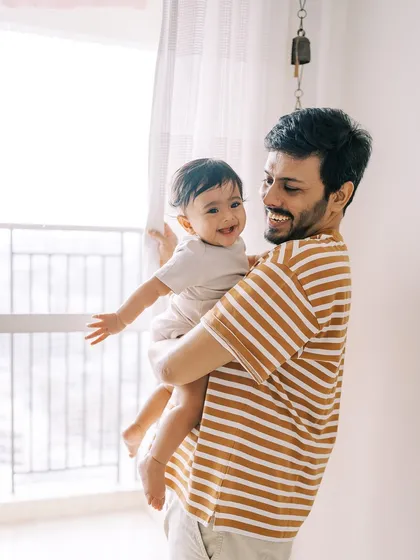 A father holding his happy nine-month-old by the window. The natural light creates a beautiful, soft portrait.