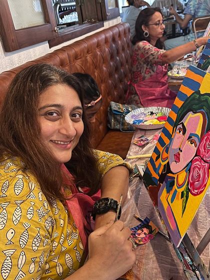A smiling participant at a coffee and paint workshop, adding color to her abstract portrait. The atmosphere is always encouraging and fun.