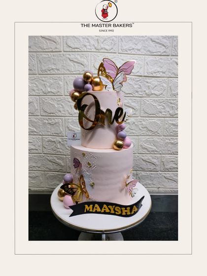 Maaysha's first birthday cake is a vision in pink and gold. This two-tiered design is adorned with elegant butterflies and a bold "One" topper, creating a sophisticated yet sweet look.