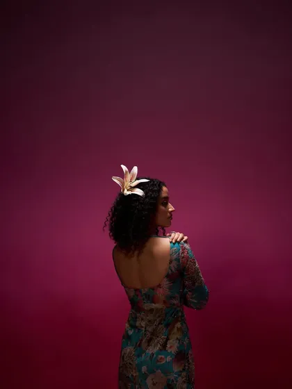 An artistic and moody shot for a clothing campaign. The makeup is minimal to suit the dramatic lighting, with a focus on the model's natural curly hair, accented with a fresh lily.