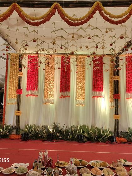 A simple yet elegant stage setup for a traditional ceremony, using columns of red and yellow flowers against a white backdrop.