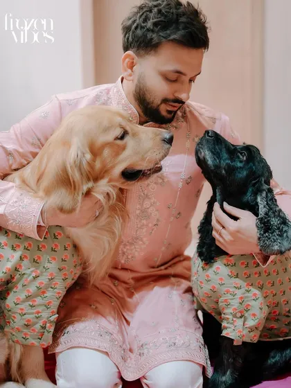 A groom shares a quiet moment with his two beloved dogs, a golden retriever and a cocker spaniel, both dressed in matching festive attire. We believe pets are family, and we love capturing these special bonds during your most important life events.