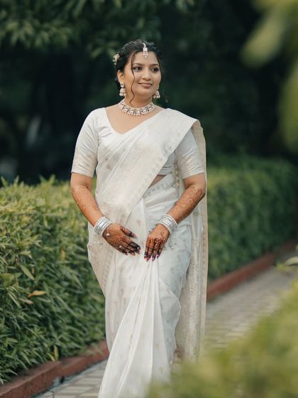 A graceful solo portrait of the bride-to-be in a beautiful white saree. Her calm and happy expression is captured perfectly amidst the natural greenery.