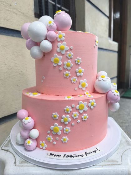 Prettiest in pink. This two-tier cake is a floral fantasy, decorated with cascading fondant daisies and clusters of pink and white baubles for a sweet and cheerful birthday.