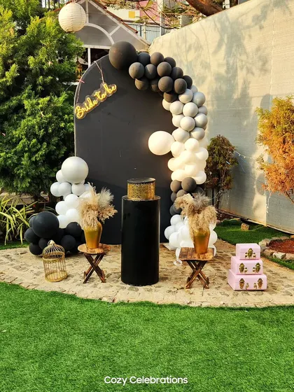 For a modern and chic bride, this black and white theme is a standout choice. The decor features a bold black backdrop with a contrasting white and black balloon arch and rustic pampas grass details.